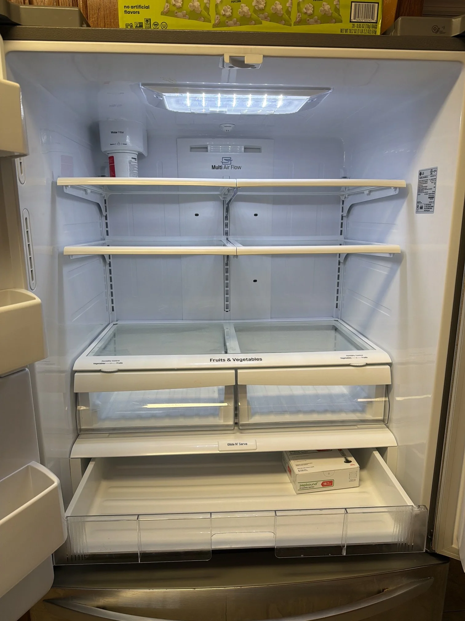 Empty refrigerator with glass shelves and a light on top, with a box of Zeepound ice packs on the bottom shelf.