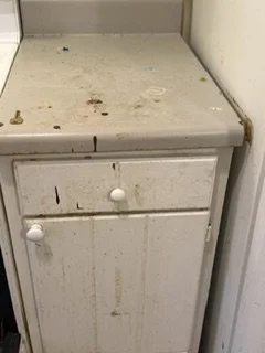 A dirty, old white kitchen or bathroom cabinet with grime and stains on the surface and around the knobs.