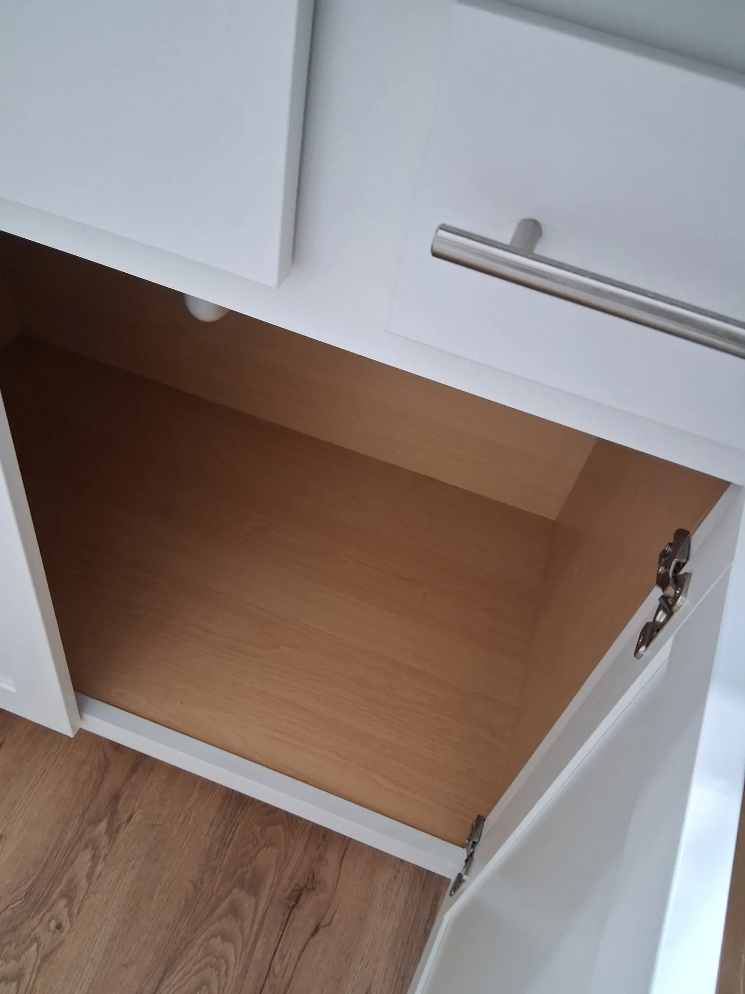 Open white cabinet with wood interior and metal hinges, standing on wood floor.