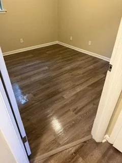Empty room with beige walls and dark wood flooring, partially open door visible.