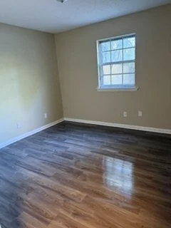 Empty room with beige walls, a window, and hardwood flooring.