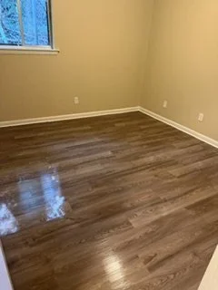 Empty room with beige walls, wooden floor, window, and electrical outlets.