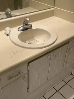 Bathroom sink with a mirror above and a damaged cabinet door below.