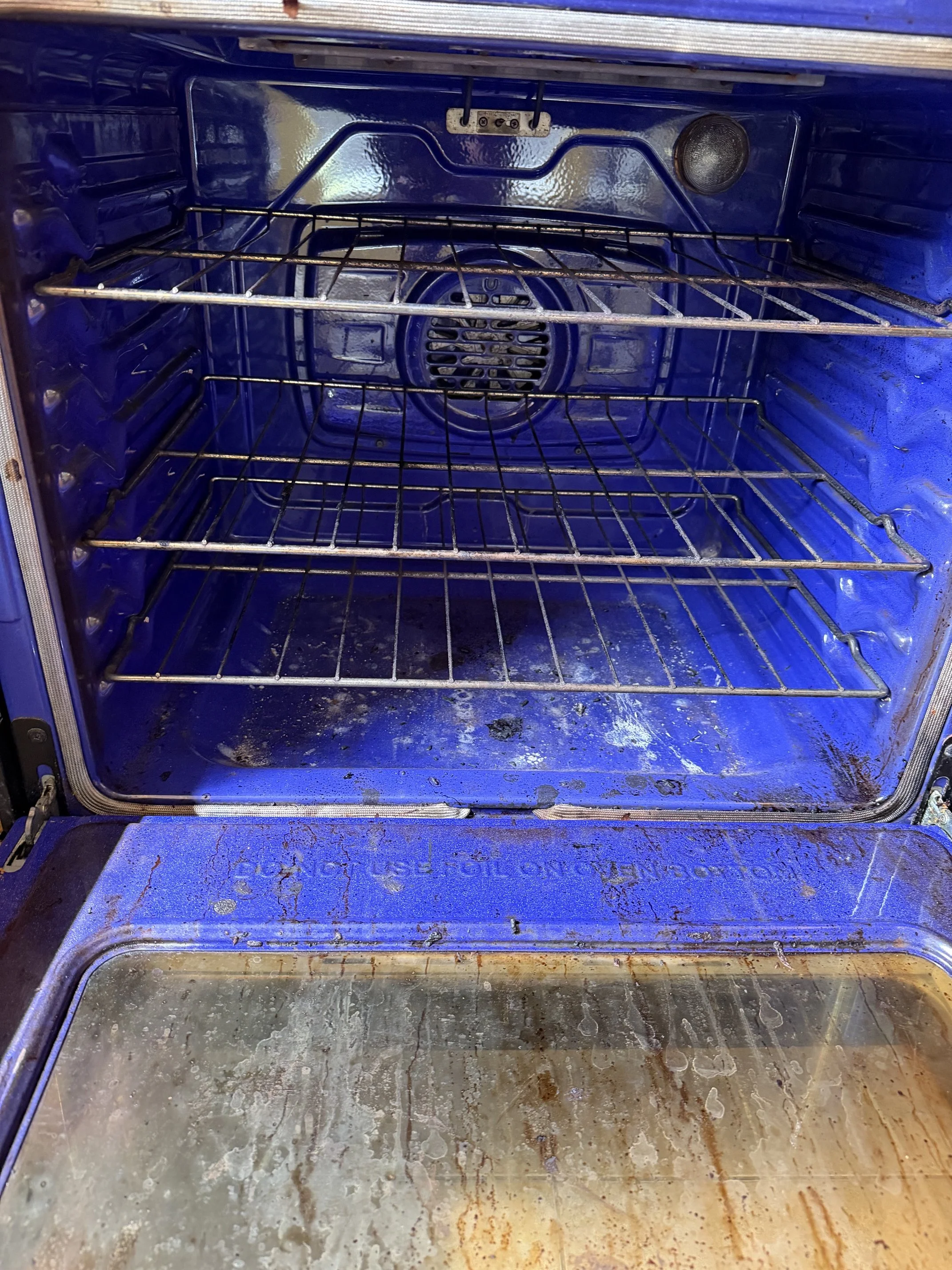 Inside of an oven with a blue interior, showing two metal racks and a dirty bottom surface with grime and stains.