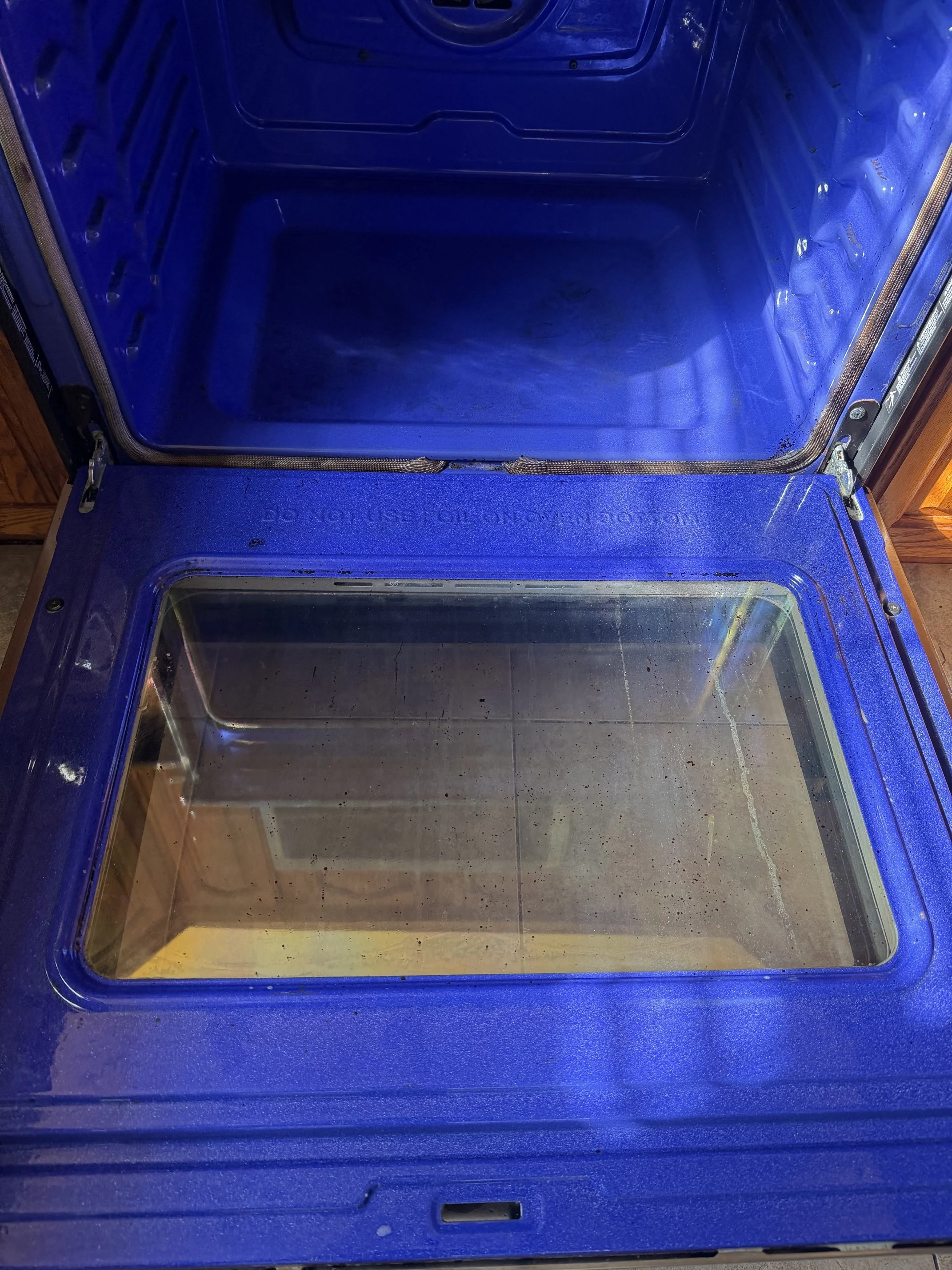 Empty blue refrigerator with a glass door, showing a blank interior and a tiled floor beneath.