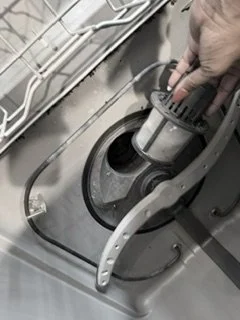 Close-up of a person's hand adjusting a component inside a dishwasher.