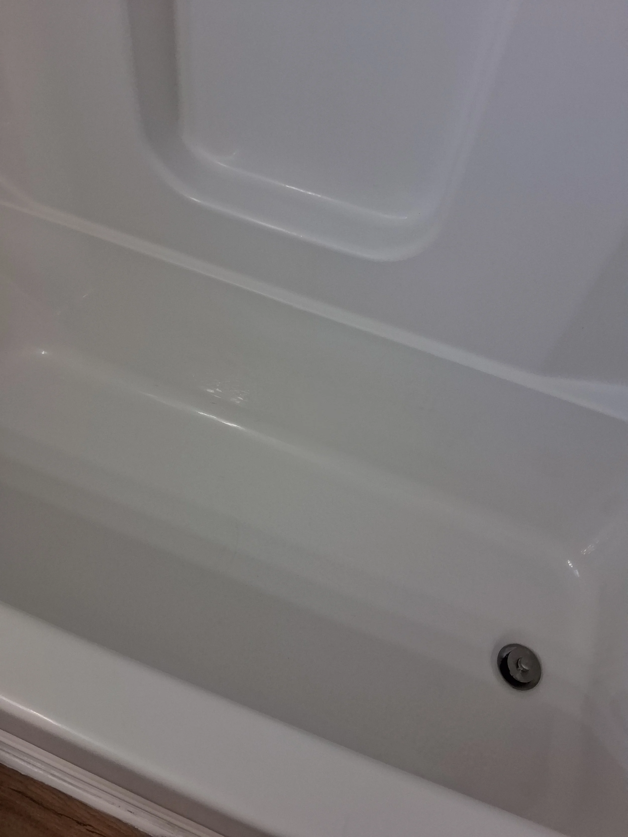 Close-up of a corner of a white bathtub with a silver drain and a shiny surface.