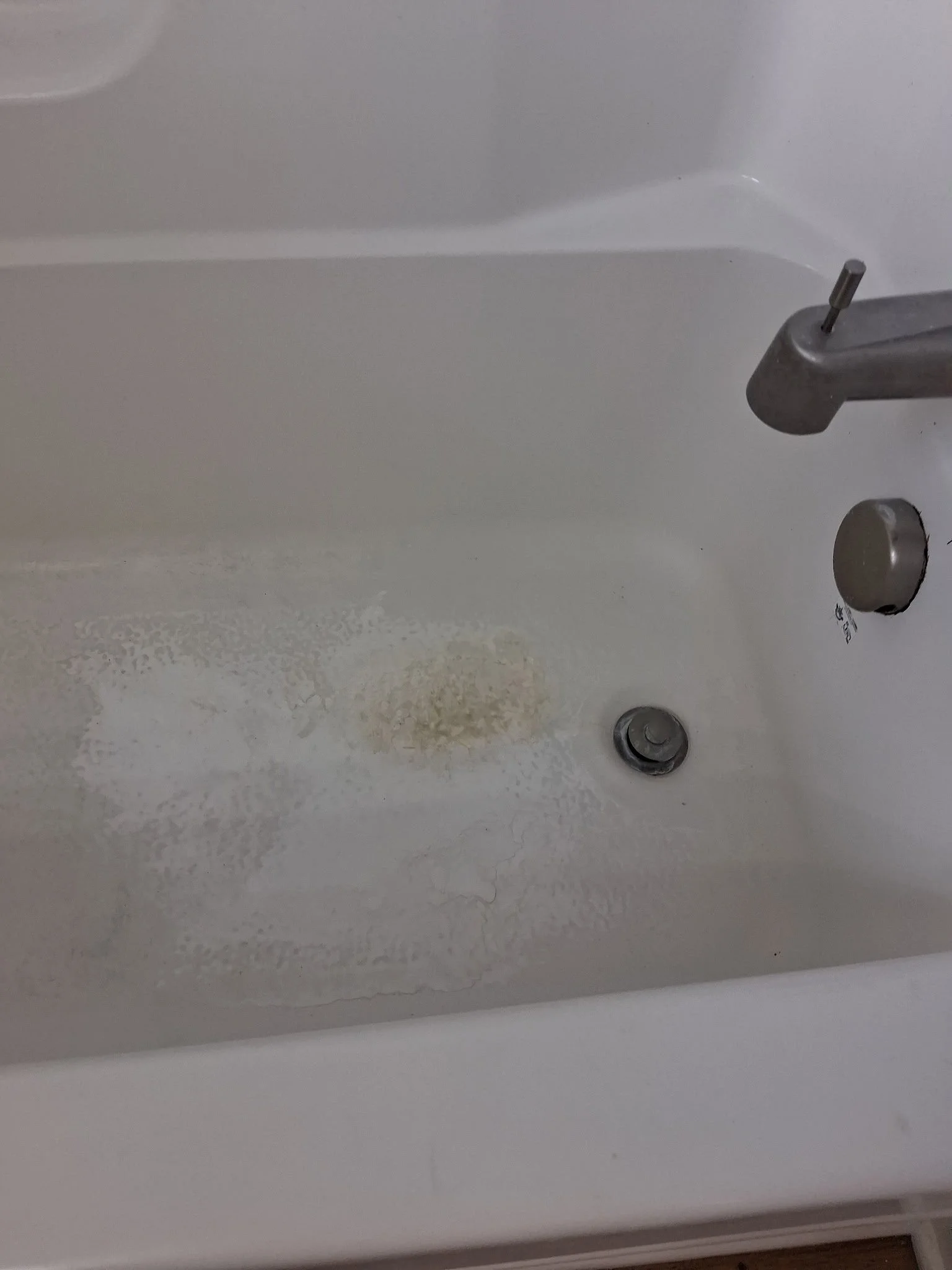 Close-up of a white bathtub with a silver faucet and drain, showing water stains and cracks on the surface.