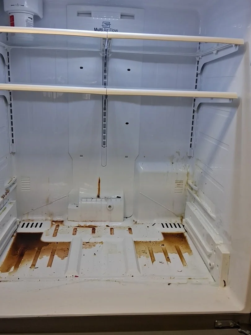 Empty refrigerator with rust stains and dirt inside, two white shelves, and missing shelves or drawers at the bottom.