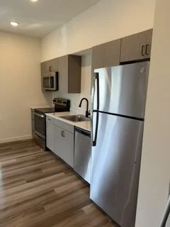Modern kitchen with stainless steel refrigerator, microwave, oven, and beige cabinets with black handles, hardwood floor.