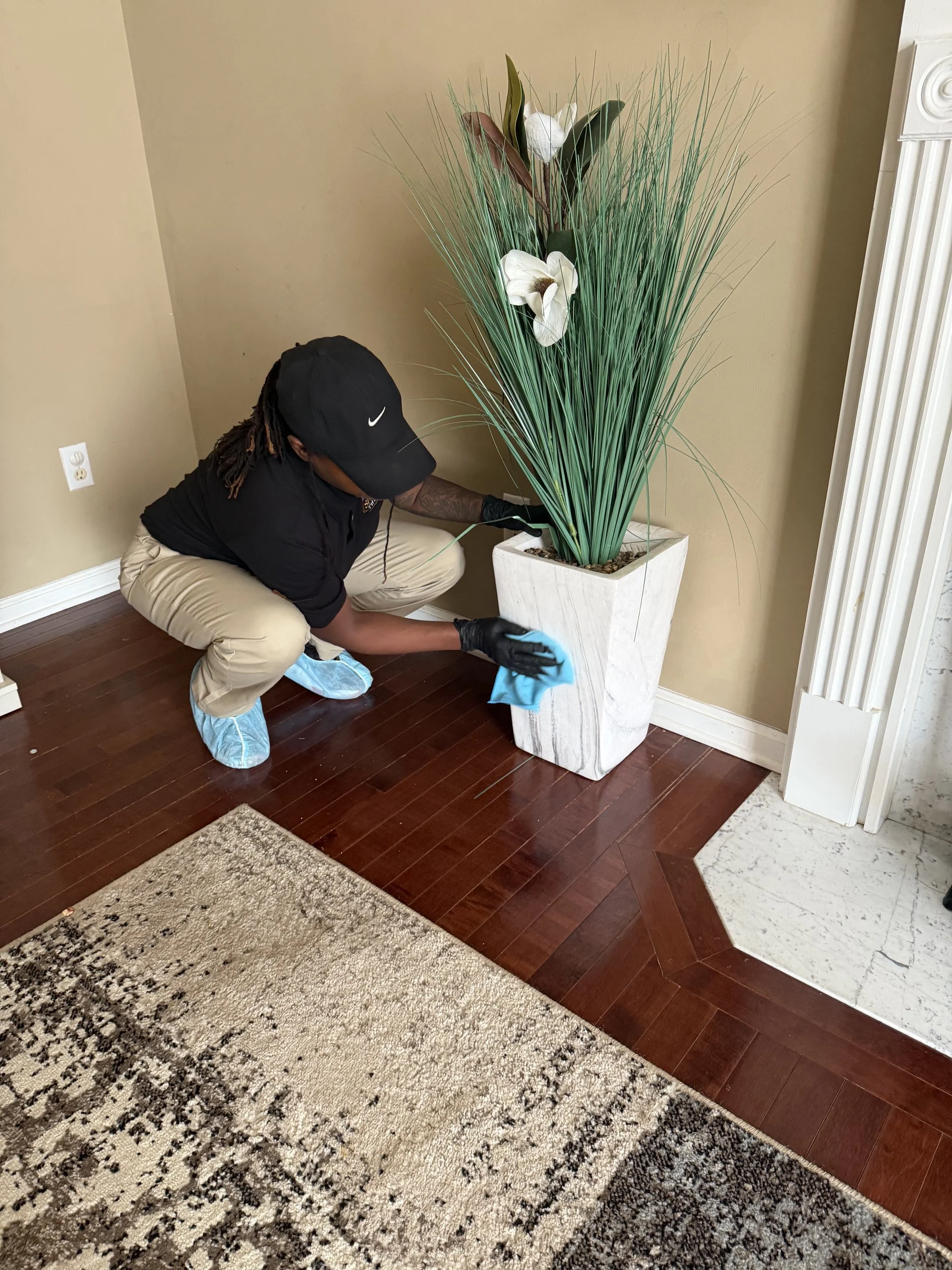 Person cleaning floor around tall potted plant in living room.