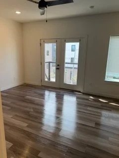 Empty room with hardwood floors, a ceiling fan, and a balcony door with glass panels leading outside.
