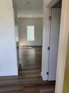 Interior view of a room with hardwood floors, a small window with sunlight, and an open door leading into another room.