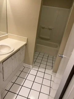 Bathroom with a sink, cabinet, and a shower stall with a door, tiled floor and walls.