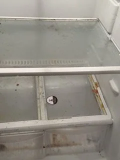 Empty glass display case in a refrigeration unit with dirt and debris inside.