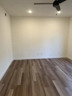 Empty room with hardwood floors, white walls, ceiling light, and a mounted black speaker or security camera.