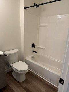 Bathroom with a toilet and bathtub, white walls, and wood-patterned flooring.