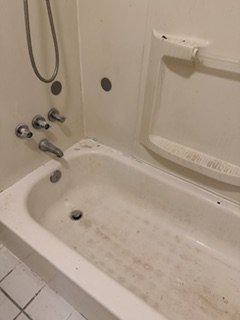 Empty bathtub with soap scum and grime, shower fixtures, and a grab bar in a bathroom.