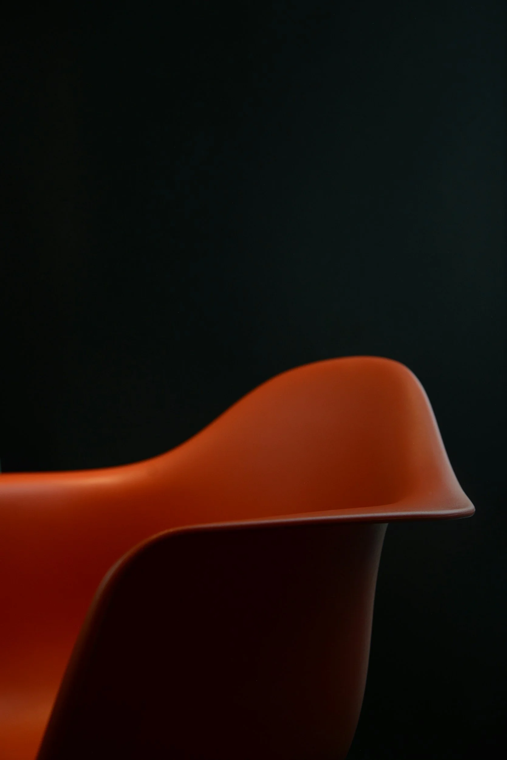 A sleek, modern orange chair with curves and smooth surfaces, set against a dark background.