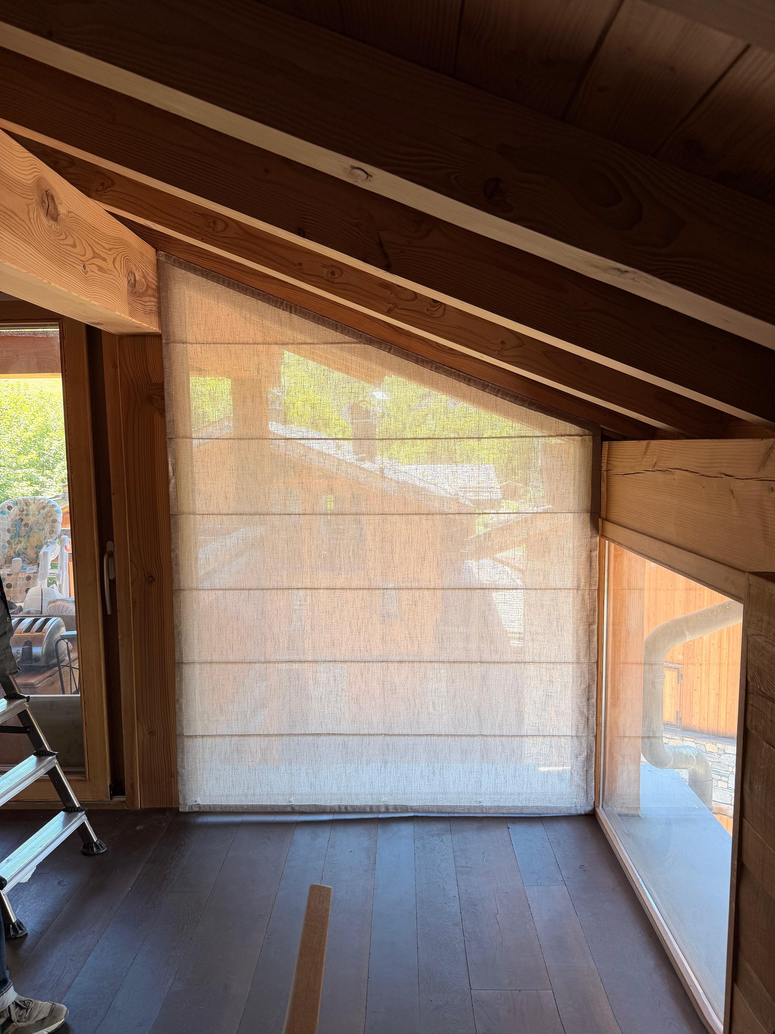 Une pièce avec des murs en bois, une grande fenêtre avec une toile transparente laissant passer la lumière naturelle, et un sol en bois foncé.