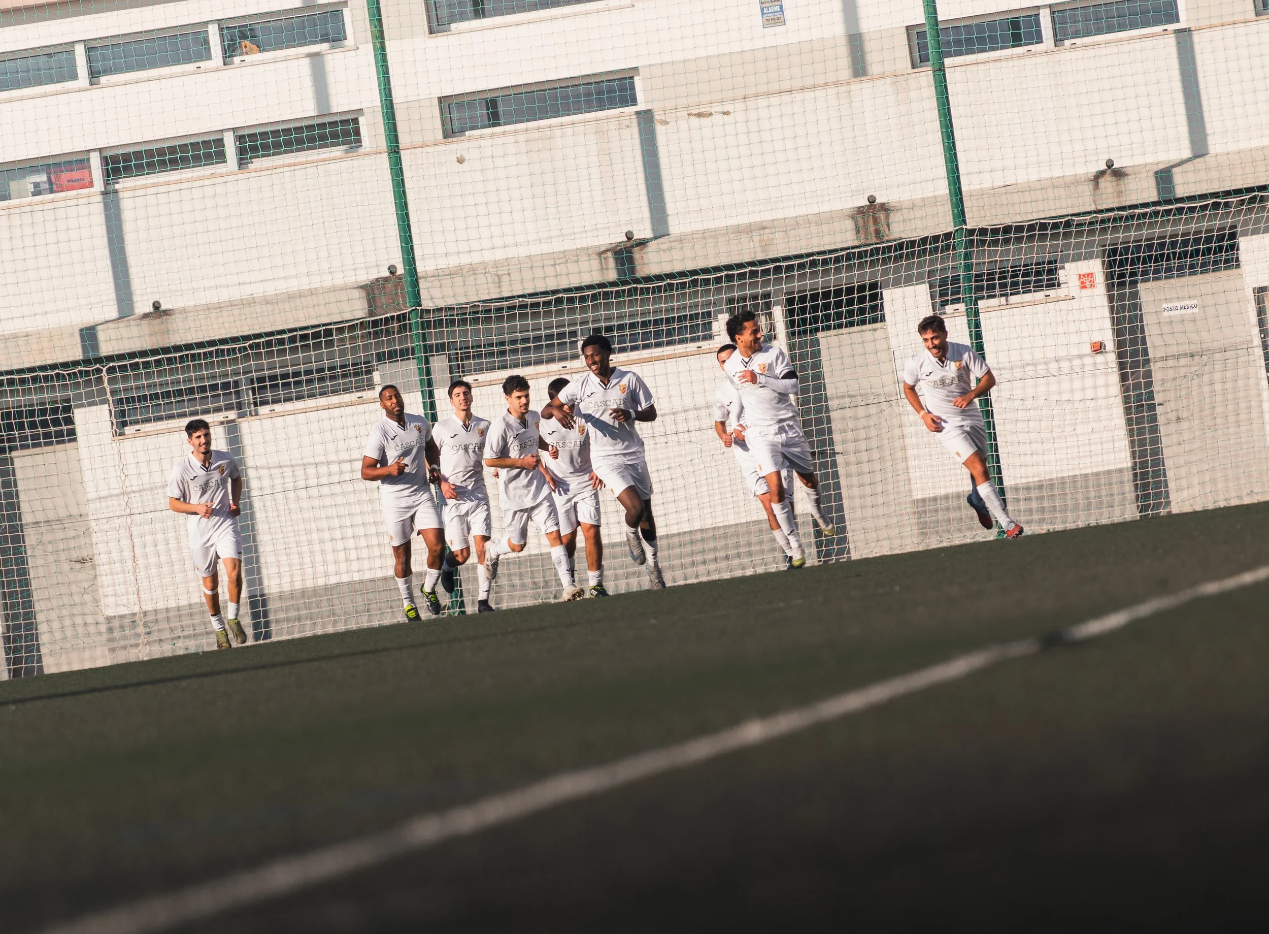 A group of football players in white uniforms running on a field during a game, celebrating a goal.