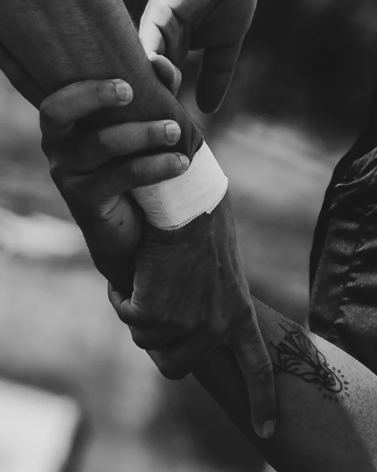 A person holding another person's hand, with a bandaged wrist and a tattoo on their forearm.
