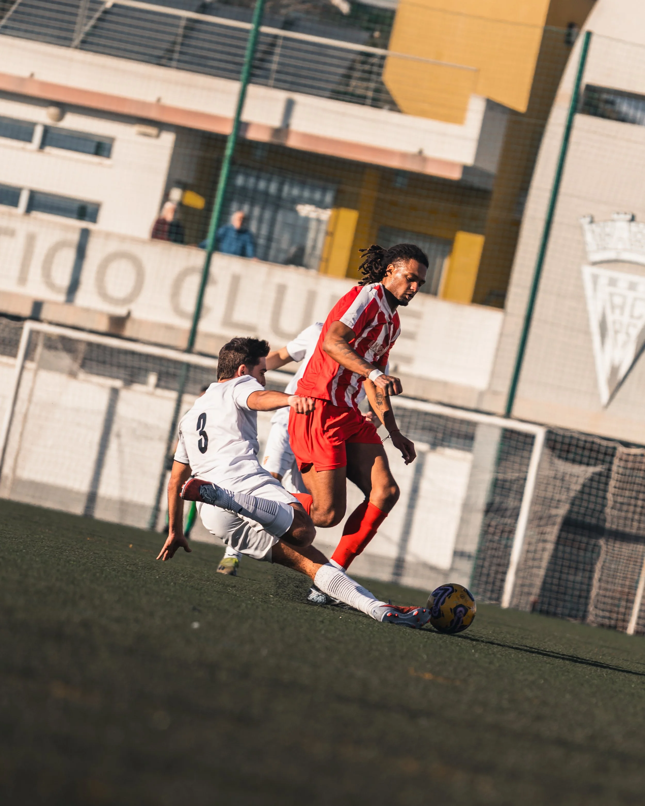 A football in a red and white uniform is about to kick a yellow and purple soccer ball on a green field. 