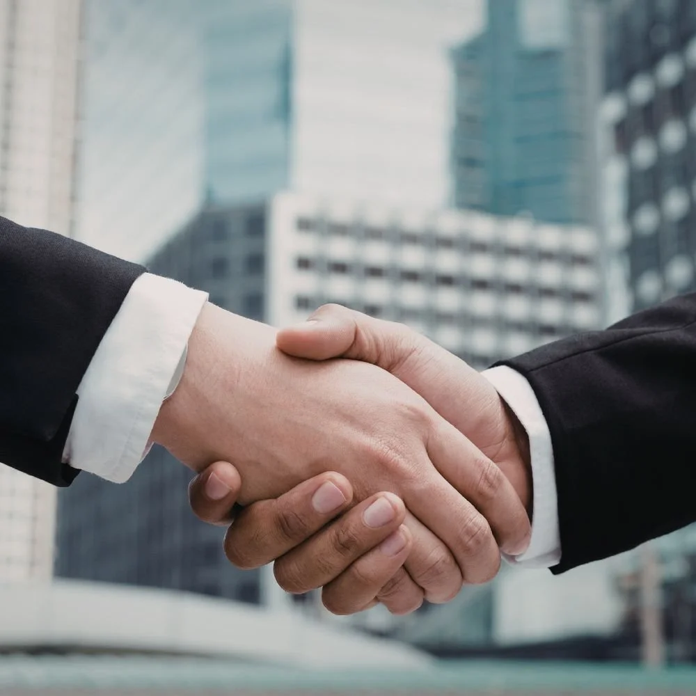 Two people shaking hands in an urban setting with skyscrapers in the background.