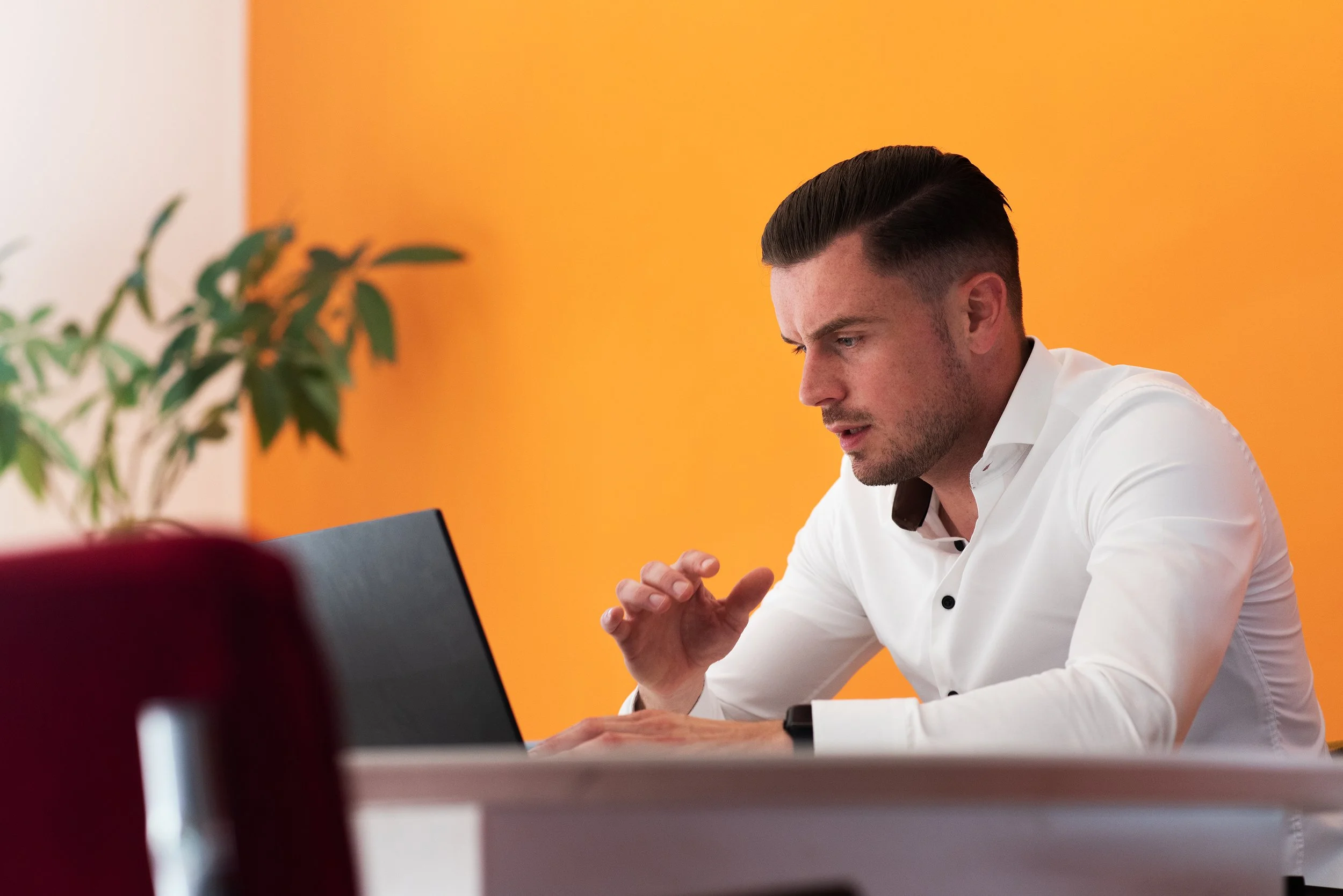 Man die geconcentreerd naar een laptop kijkt in een kantoor met een oranje muur.