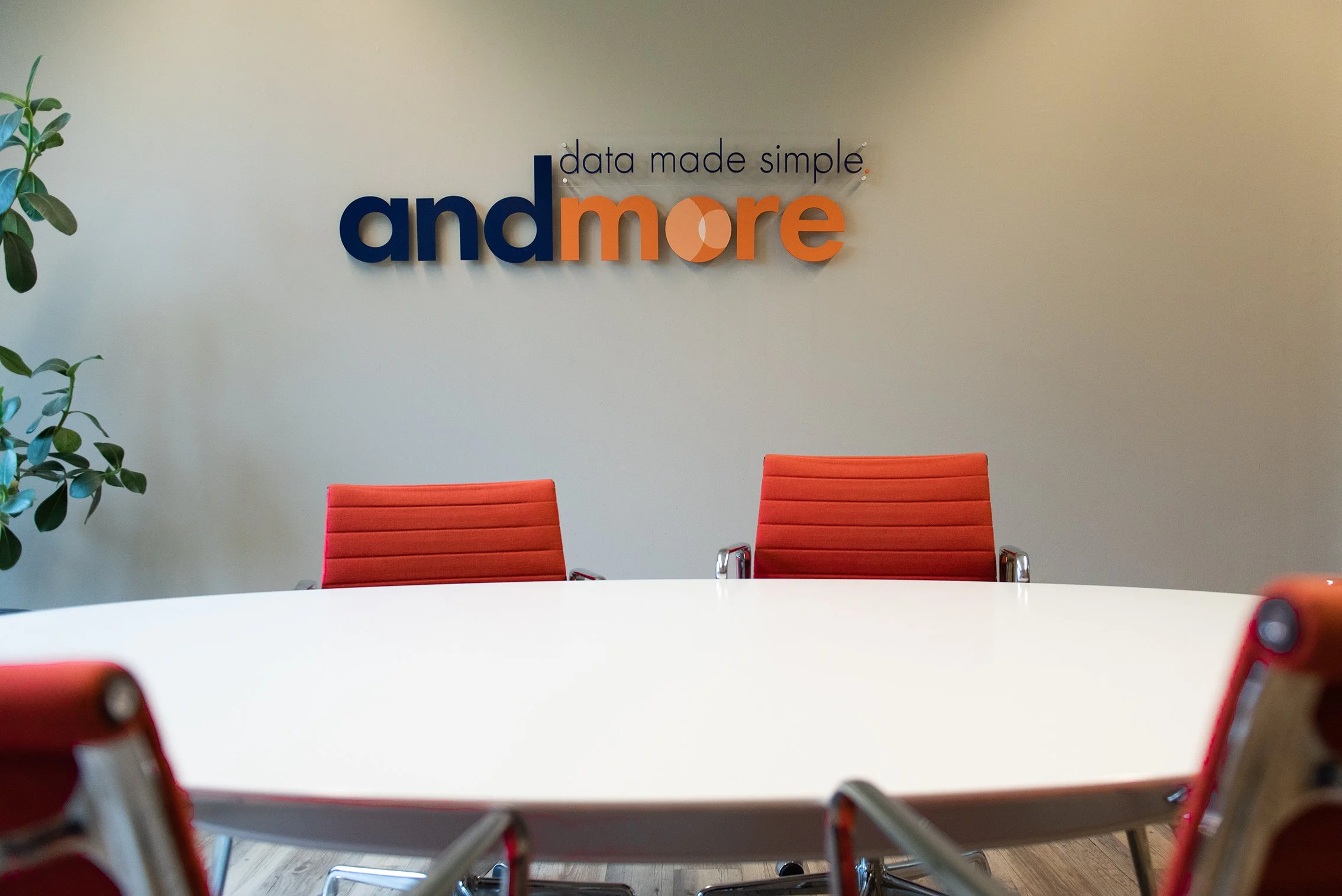 Een vergaderruimte met rode stoelen en een witte tafel, muur met een logo en slogan dat zegt "data made simple, andmore".