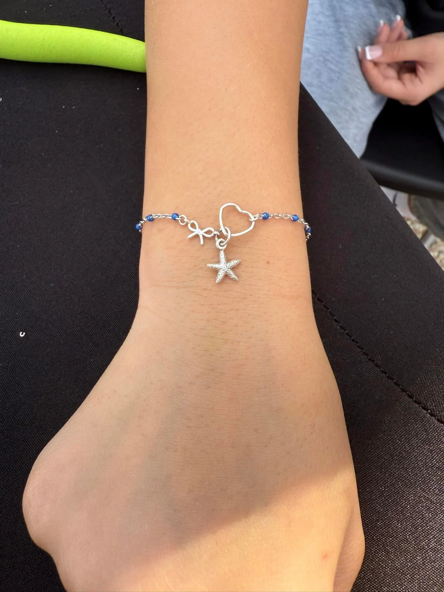 Close-up of a person's arm wearing a starfish-shaped silver bracelet with blue beads on a black fabric background.