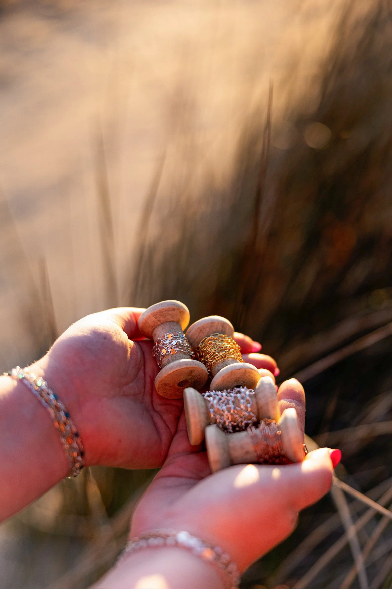 Close-up of a person's hand holding a jewelry display rack with multiple jewelry pieces, including rings and bracelets, with a blurred background of a fence or grid.