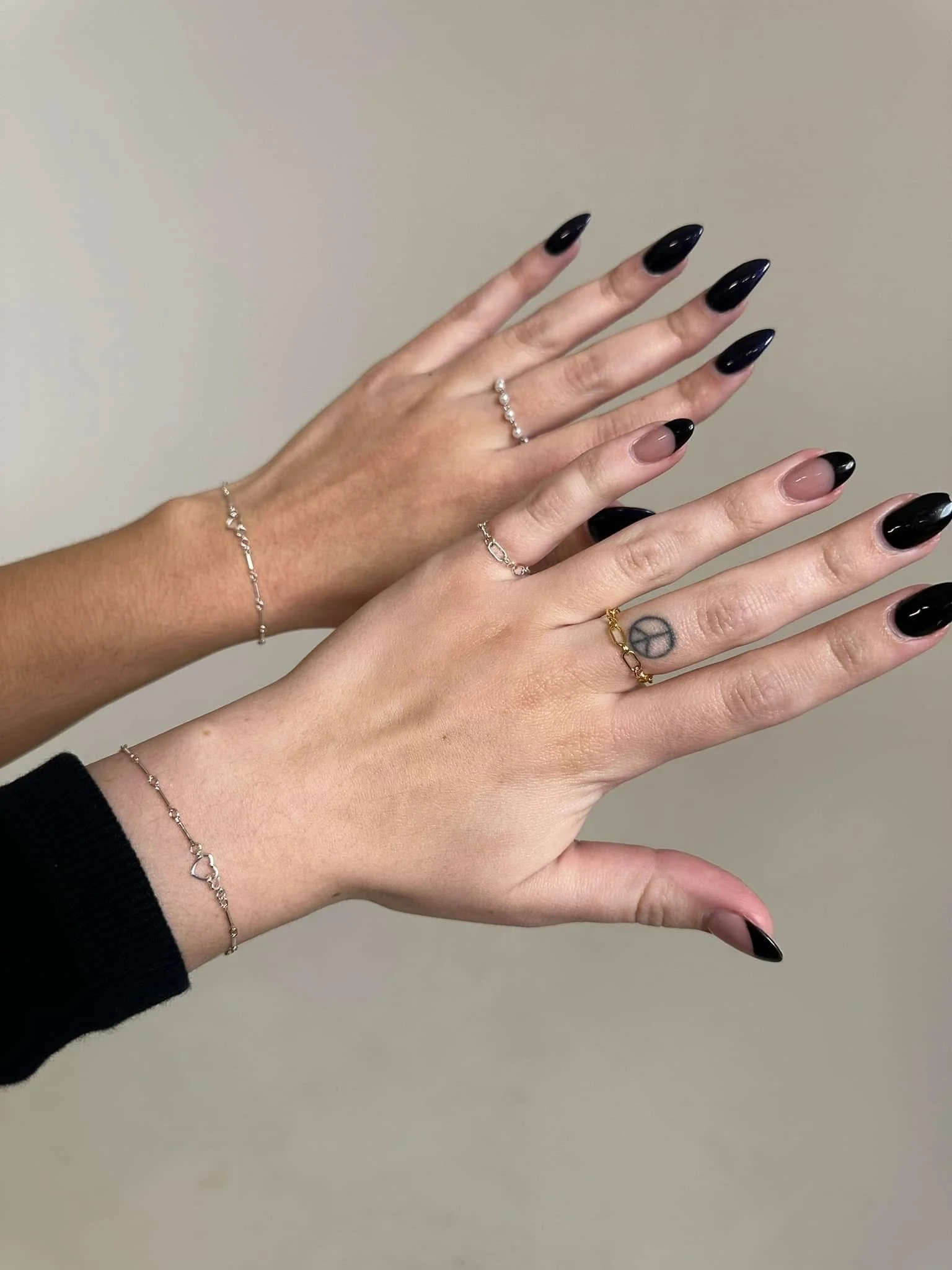 Two hands with different skin tones displaying rings and bracelets, against a plain background.