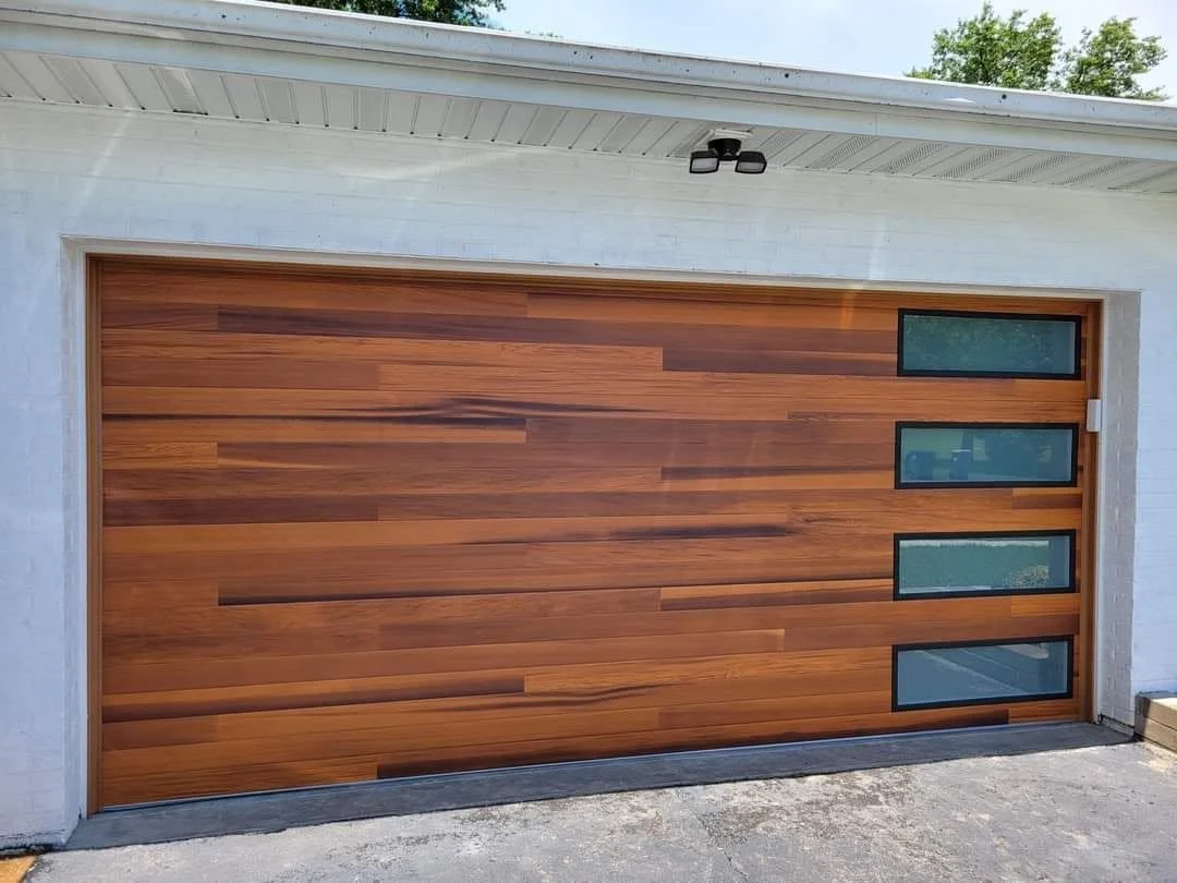 Wooden garage door with four small horizontal windows on the upper right side, set in a white brick wall with vented soffit and security light above.
