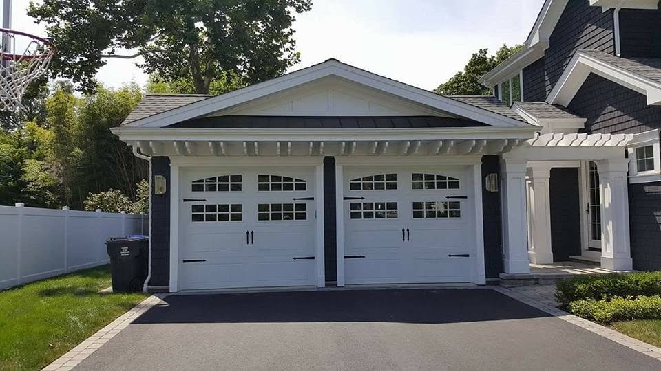 Front view of a detached garage with white doors and black accents, part of a modern house with a dark gray exterior and white trim.