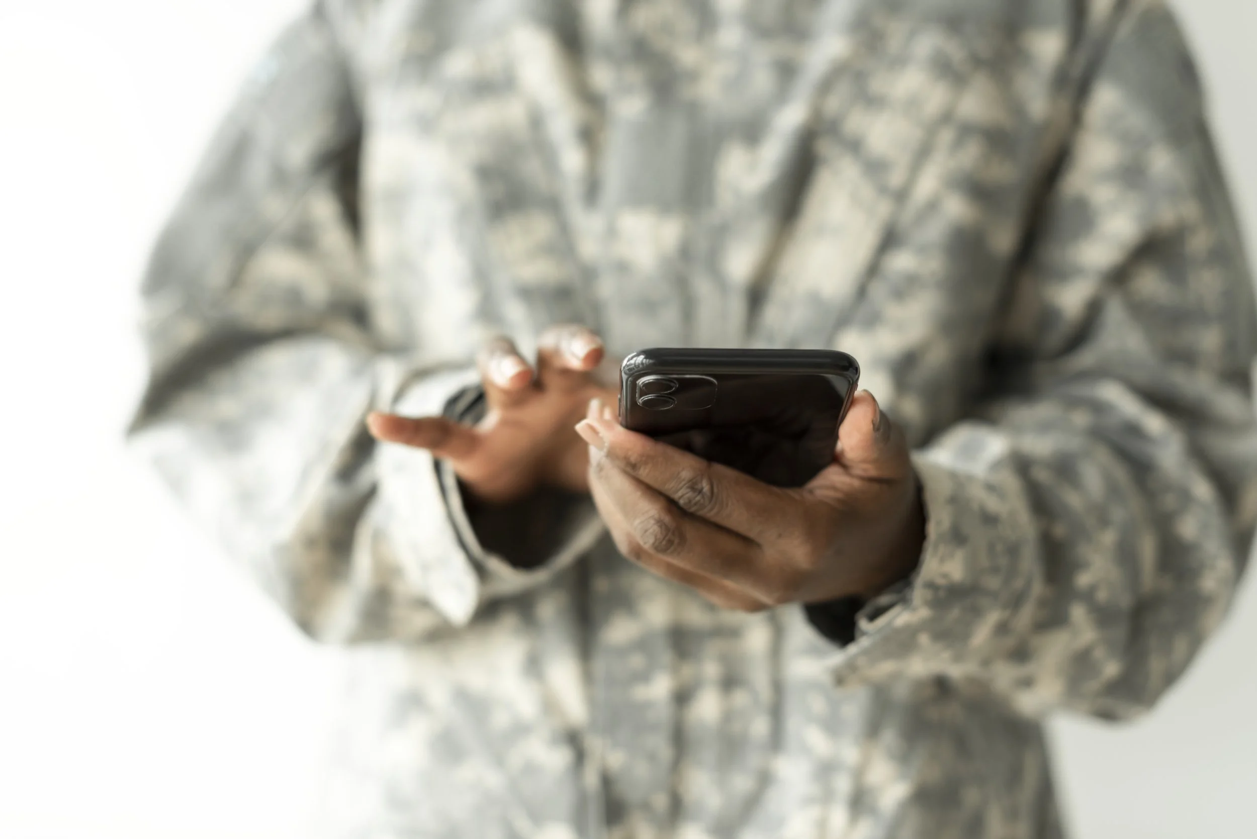 Person holding a smartphone with a blurred camouflage jacket.
