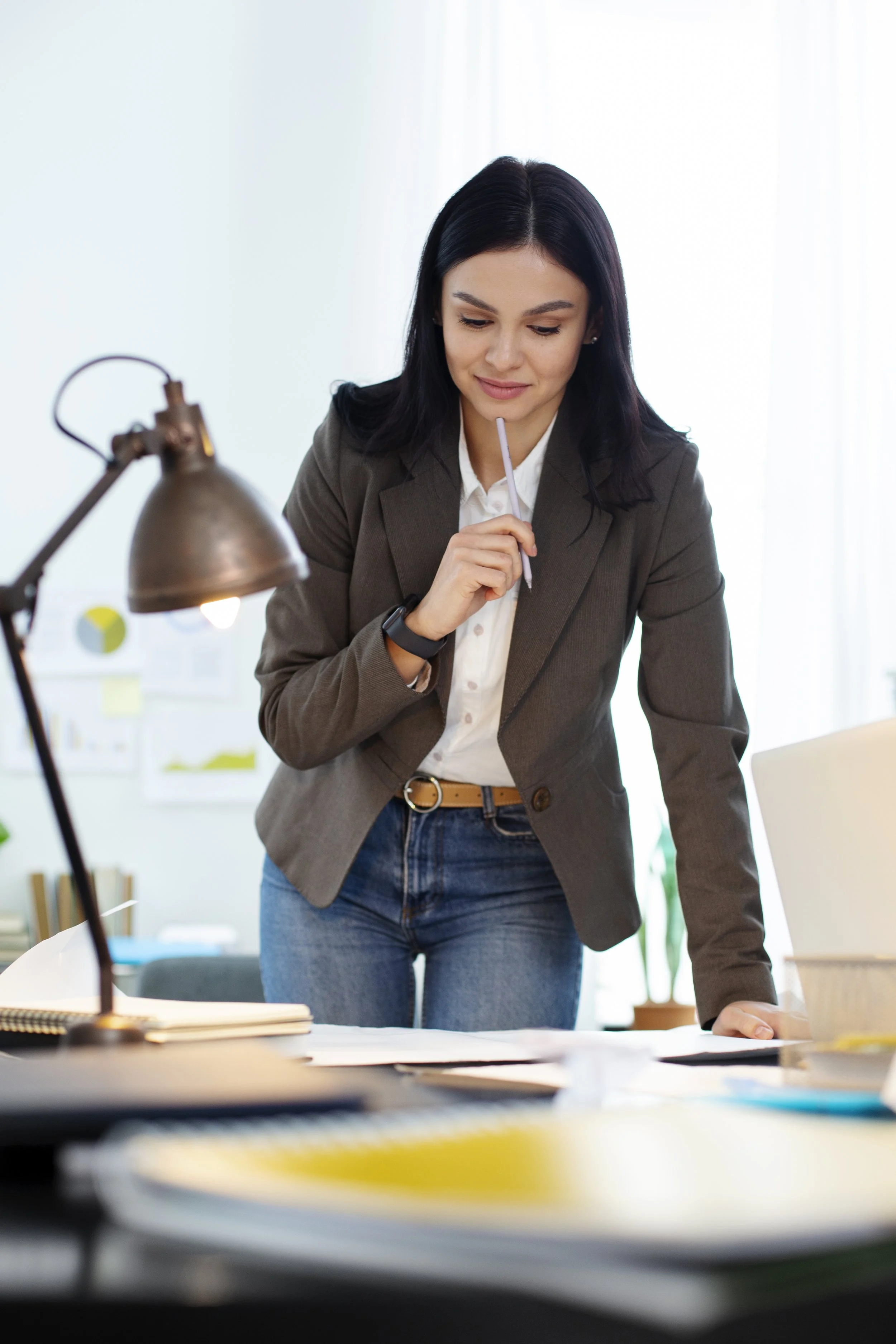 Woman in business casual attire reviewing documents on a desk in an office.