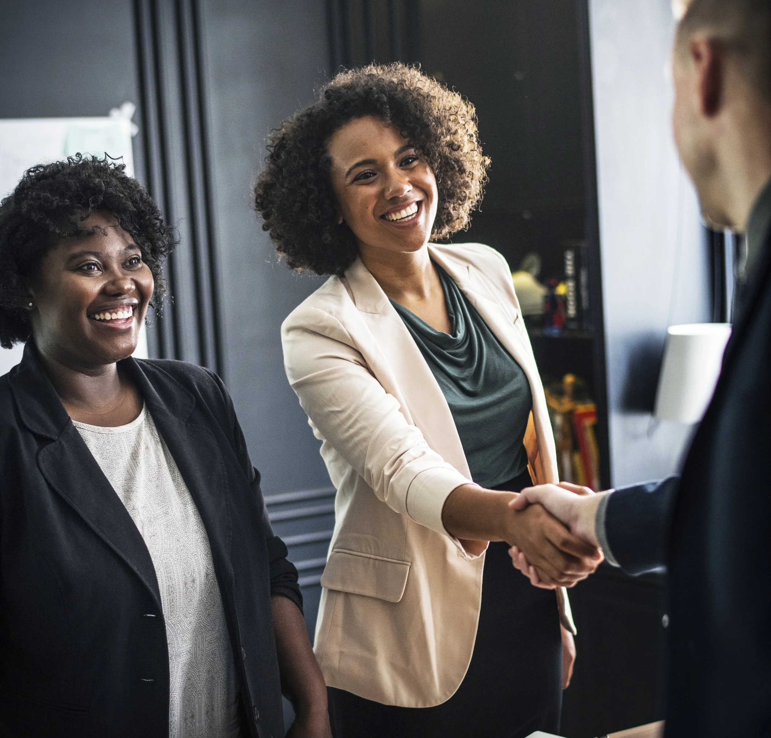 Two women smiling and shaking hands during a business meeting.