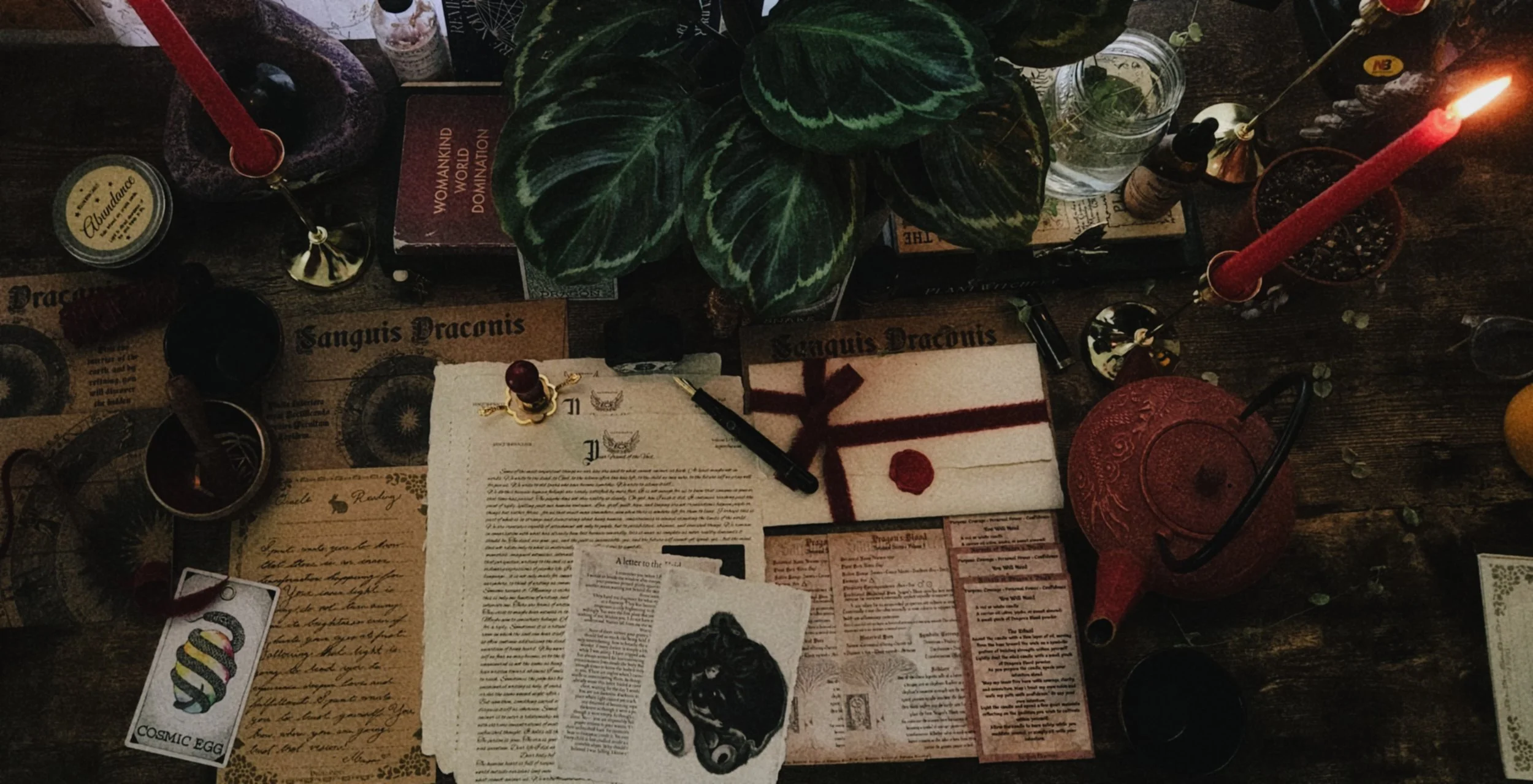 A flat lay of mystical and religious items on a wooden surface, including candles, books, botanical leaves, papers, a crystal, a lamp, and various small objects.