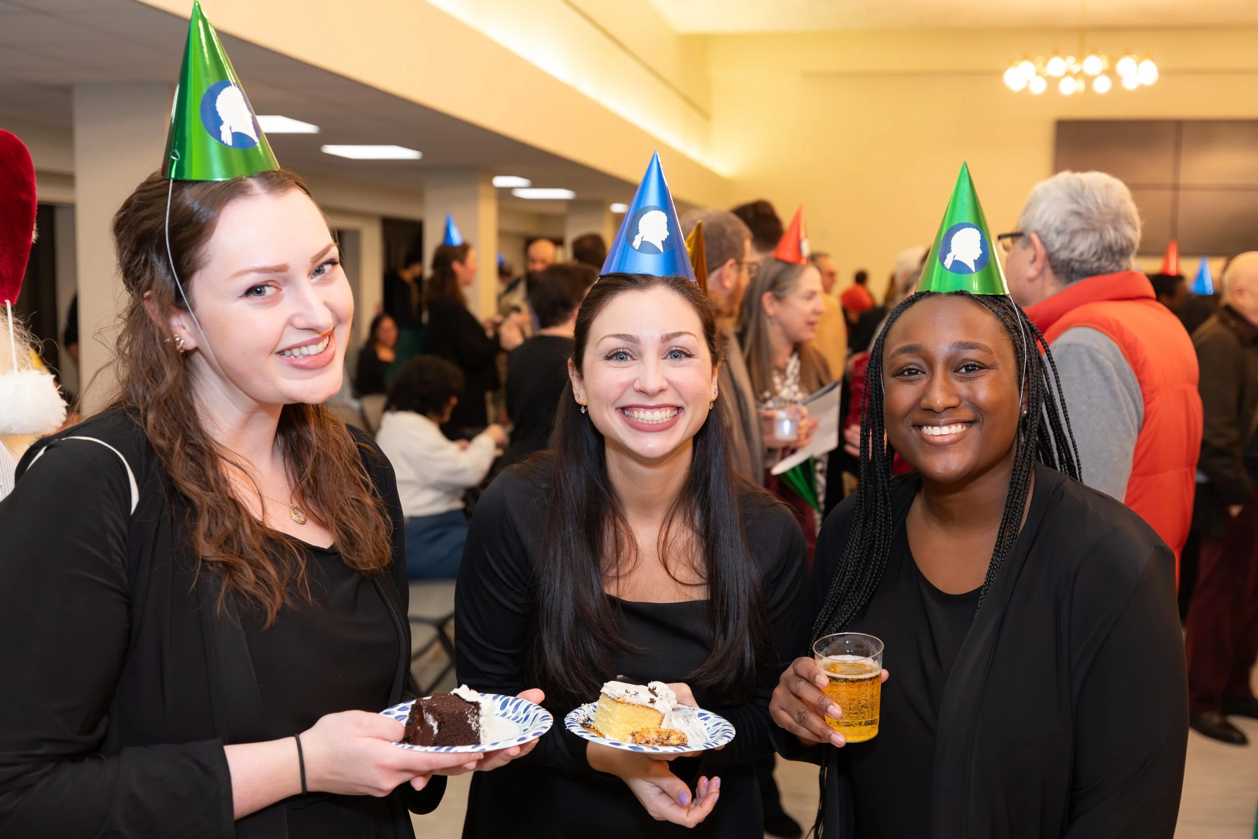 Three smiling choristers in party hats at a post-concert reception.