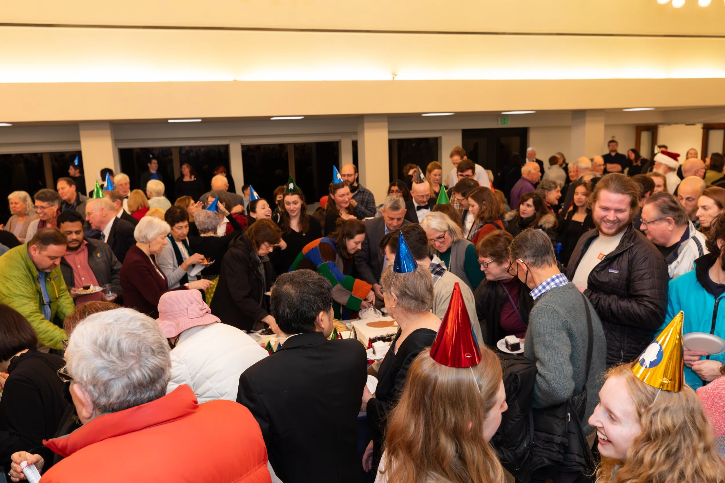 A crowd of people at a post-concert reception. some wearing party hats.