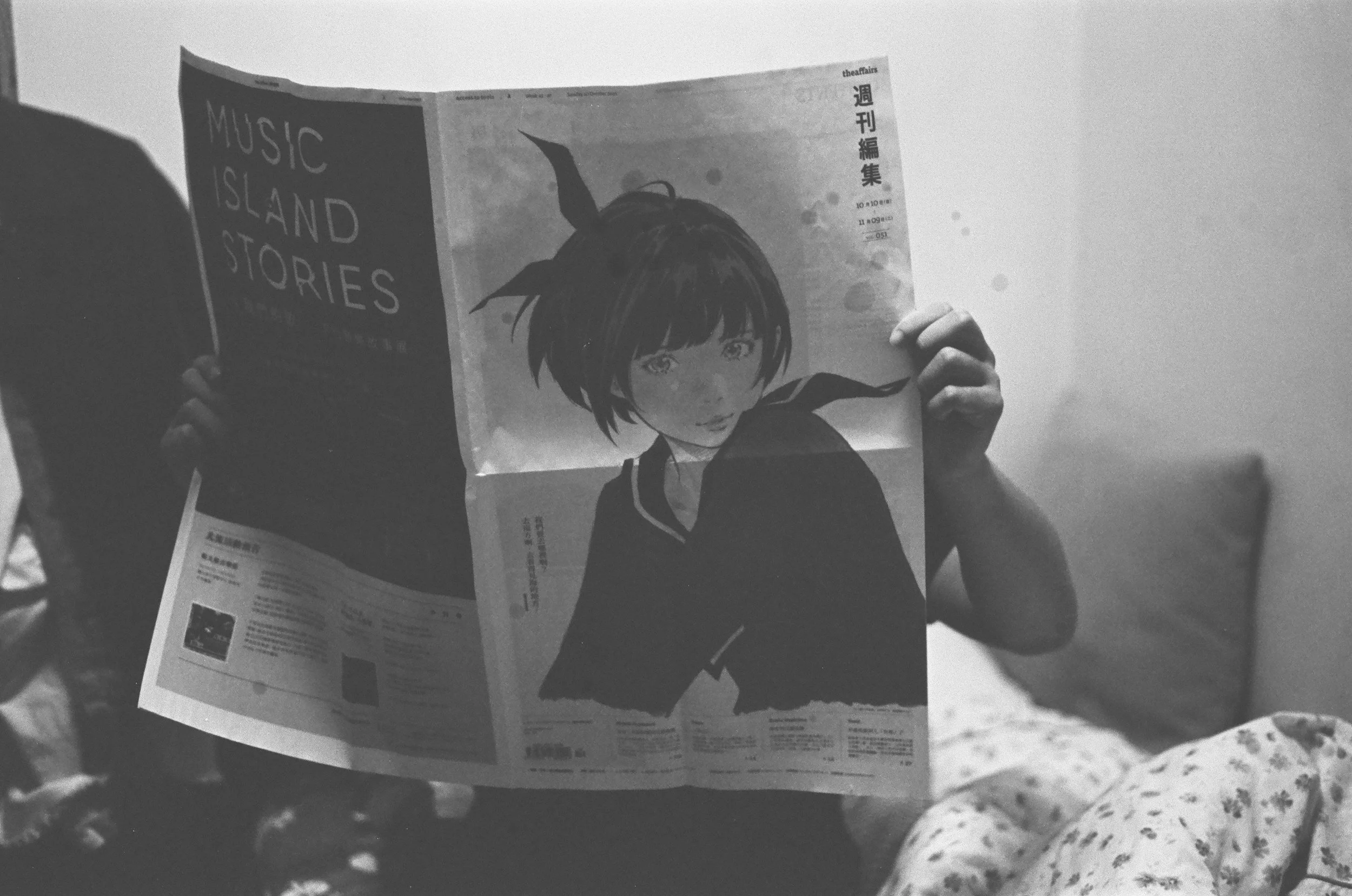 Personne lisant un journal avec une couverture illustrée d'une jeune fille avec des cheveux courts et une veste noire, en noir et blanc.