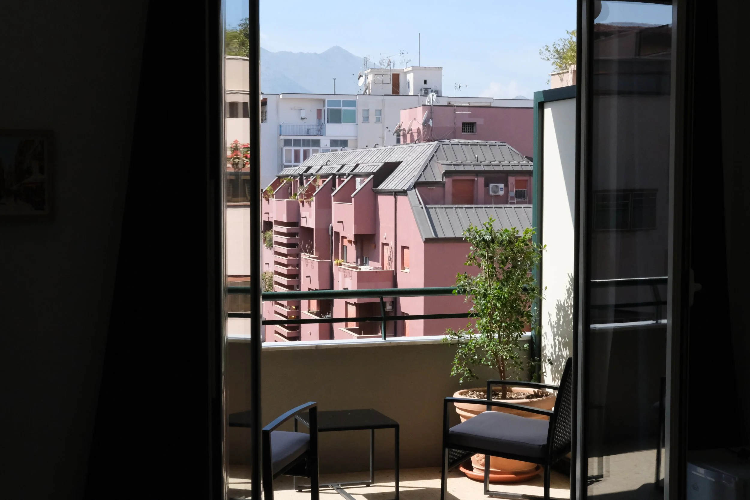 Vista da una finestra di un edificio con palazzi colorati e montagne sullo sfondo.