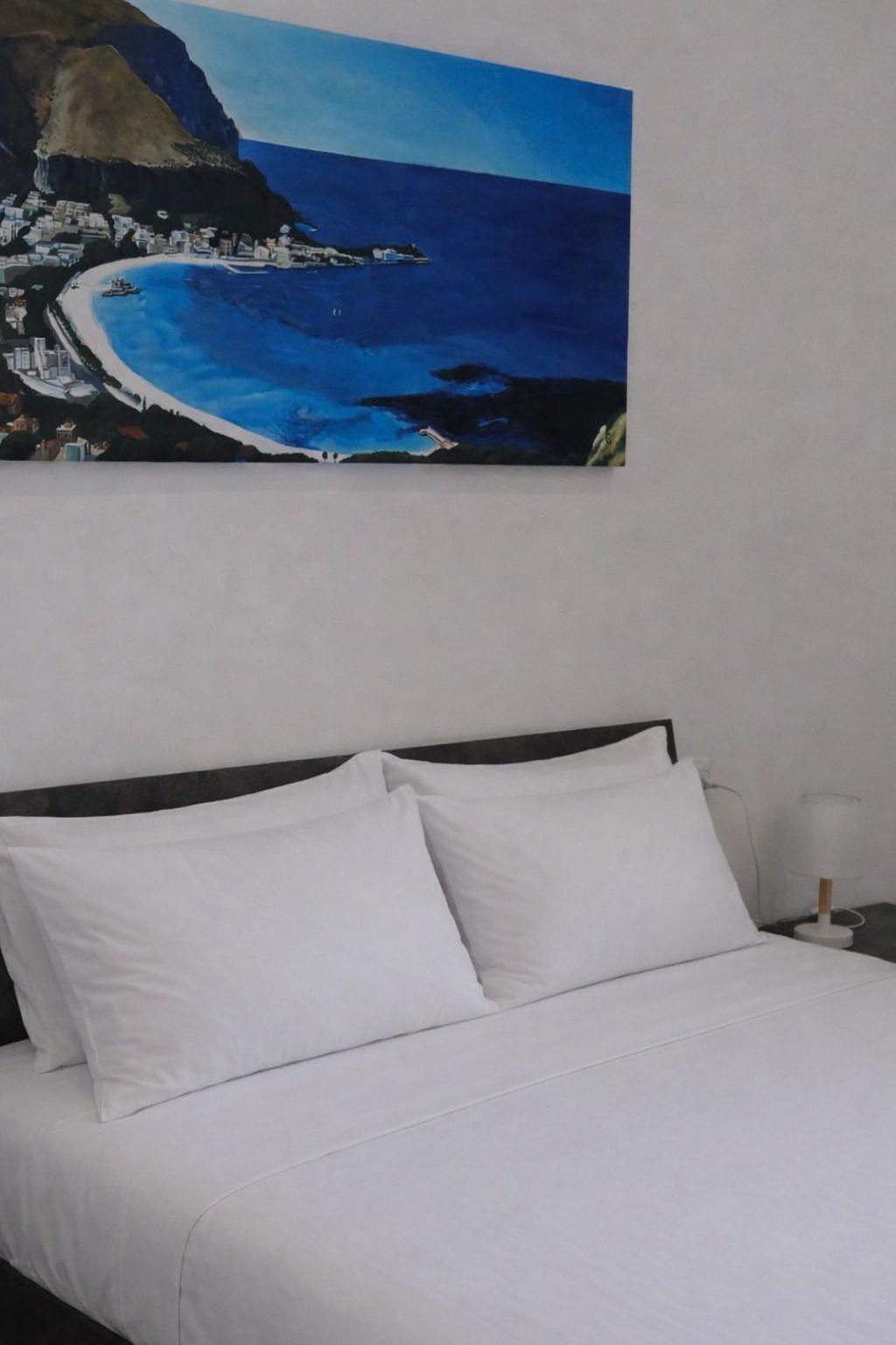 Letto con cuscini bianchi e quadro con paesaggio costiero alle spalle