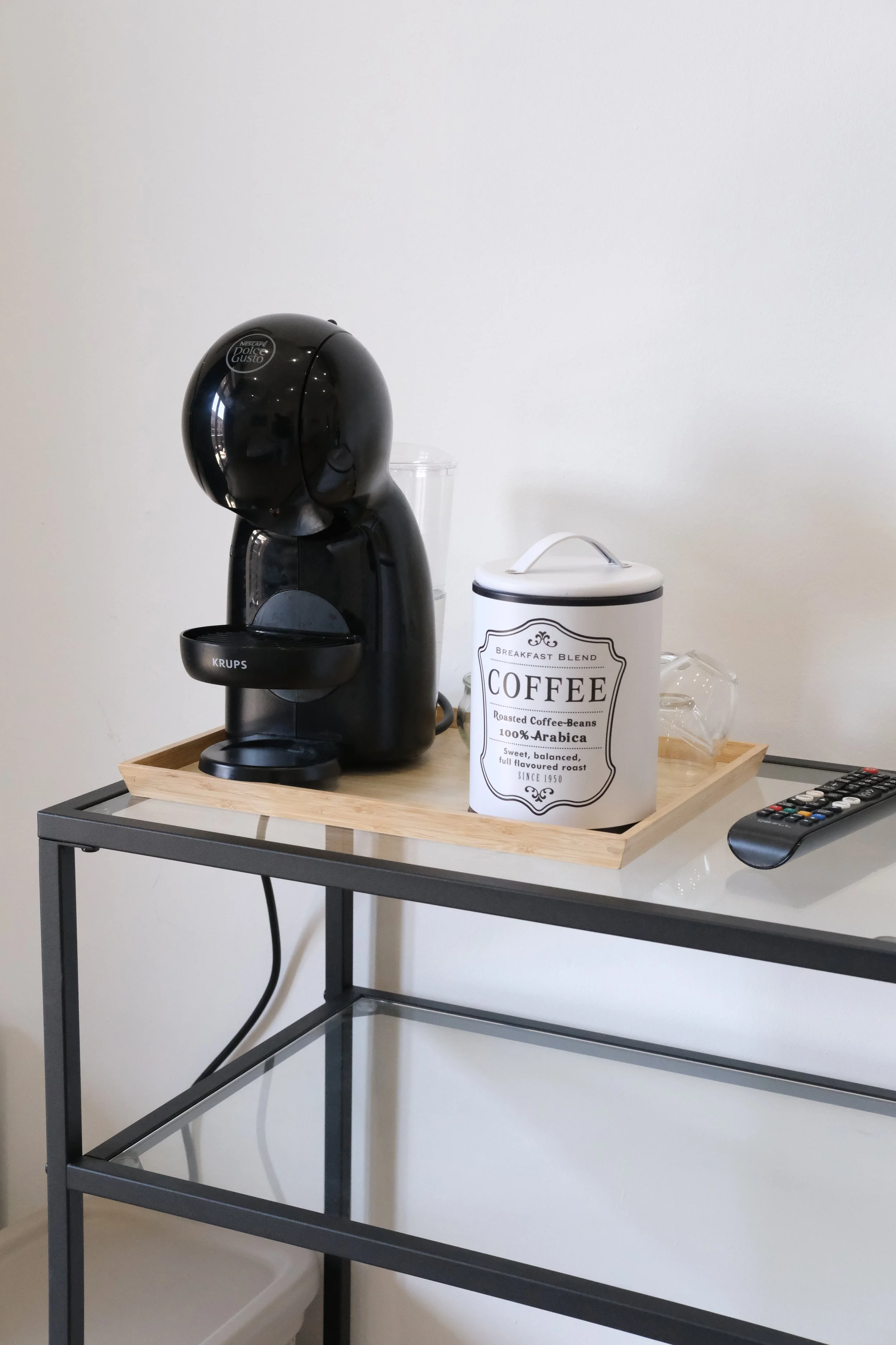 Macchina per il caffè Nescafé Dolce Gusto su un tavolo con una scatola di caffè, un bicchiere di plastica, e un telecomando