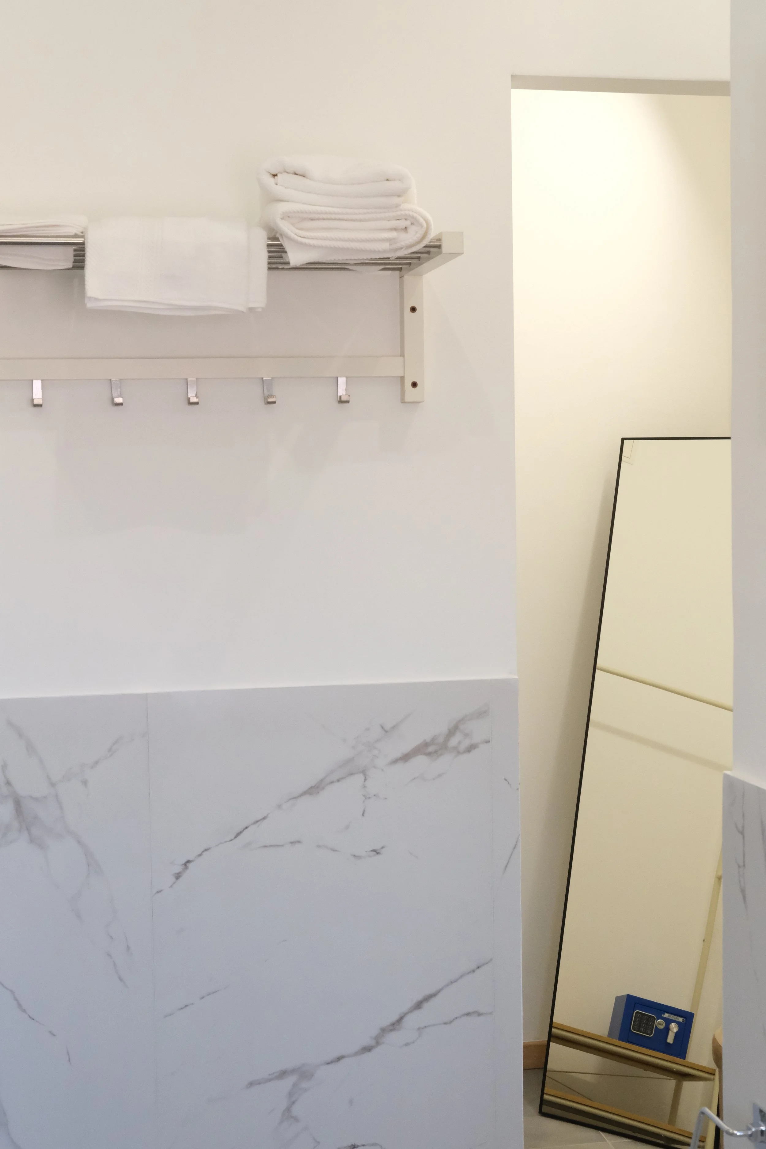 Specchio, parete bianca, panca in legno con cassetti, un telecomando e un mini scaffale in legno con lucchetto digitale.