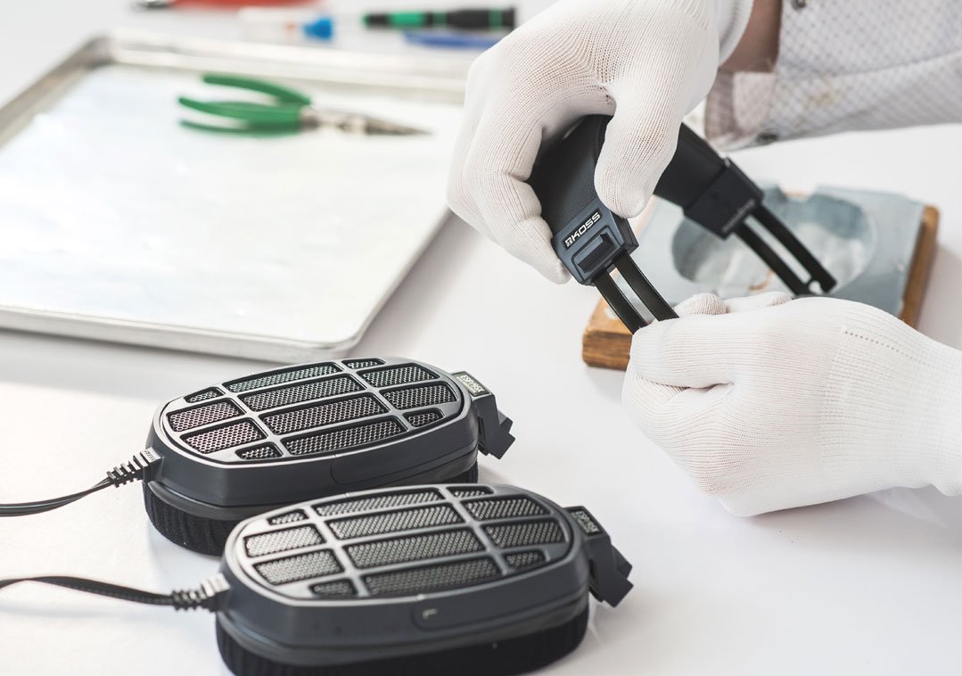 Person wearing white gloves working with electrostatic headphones on a white work surface.