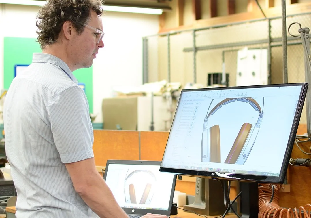 Man in a white shirt working on a computer with a design of headphones displayed on the monitor.