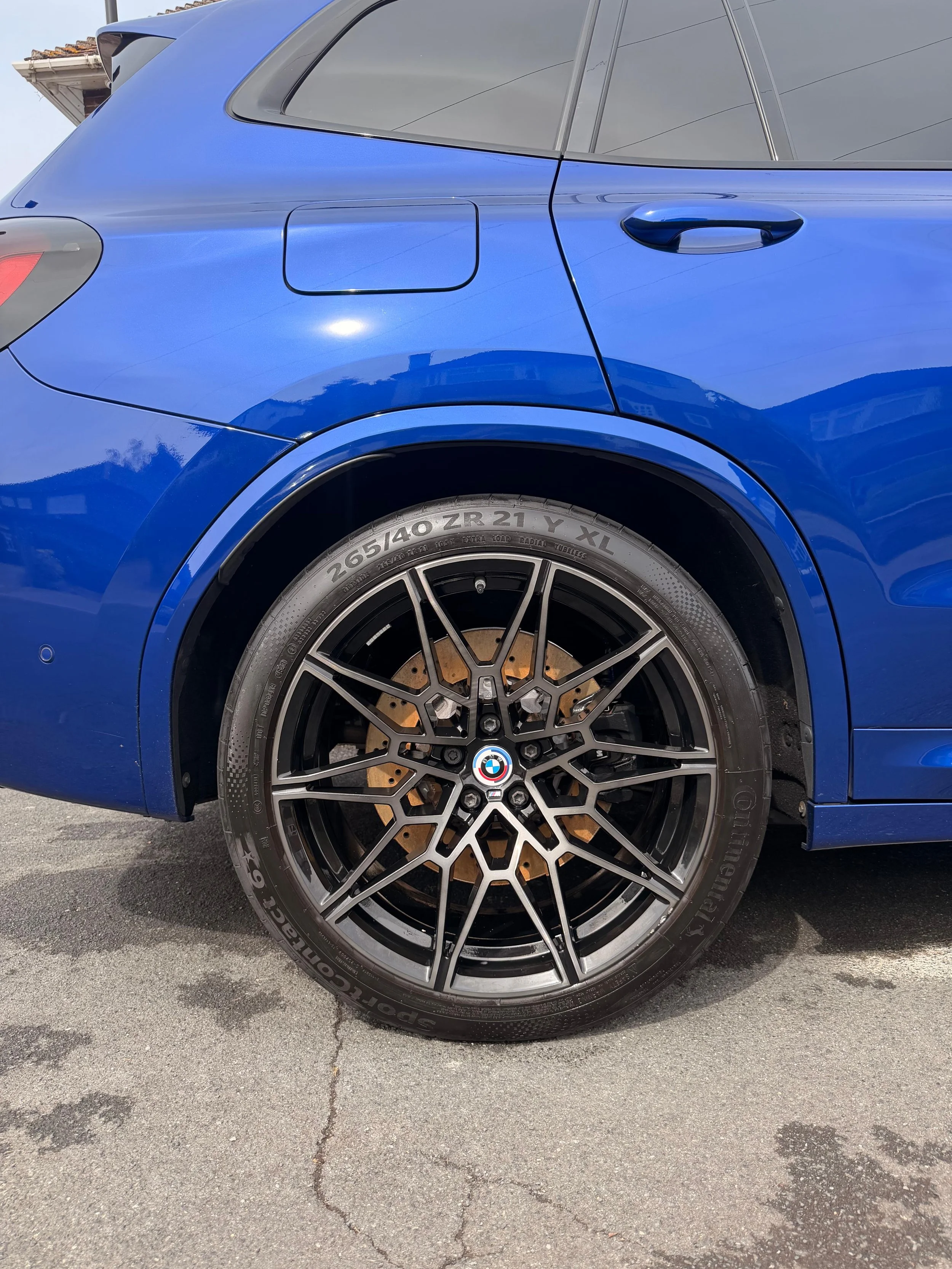 Close-up of the rear side of a blue BMW SUV, showing the wheel with a black and silver rim and the tire.