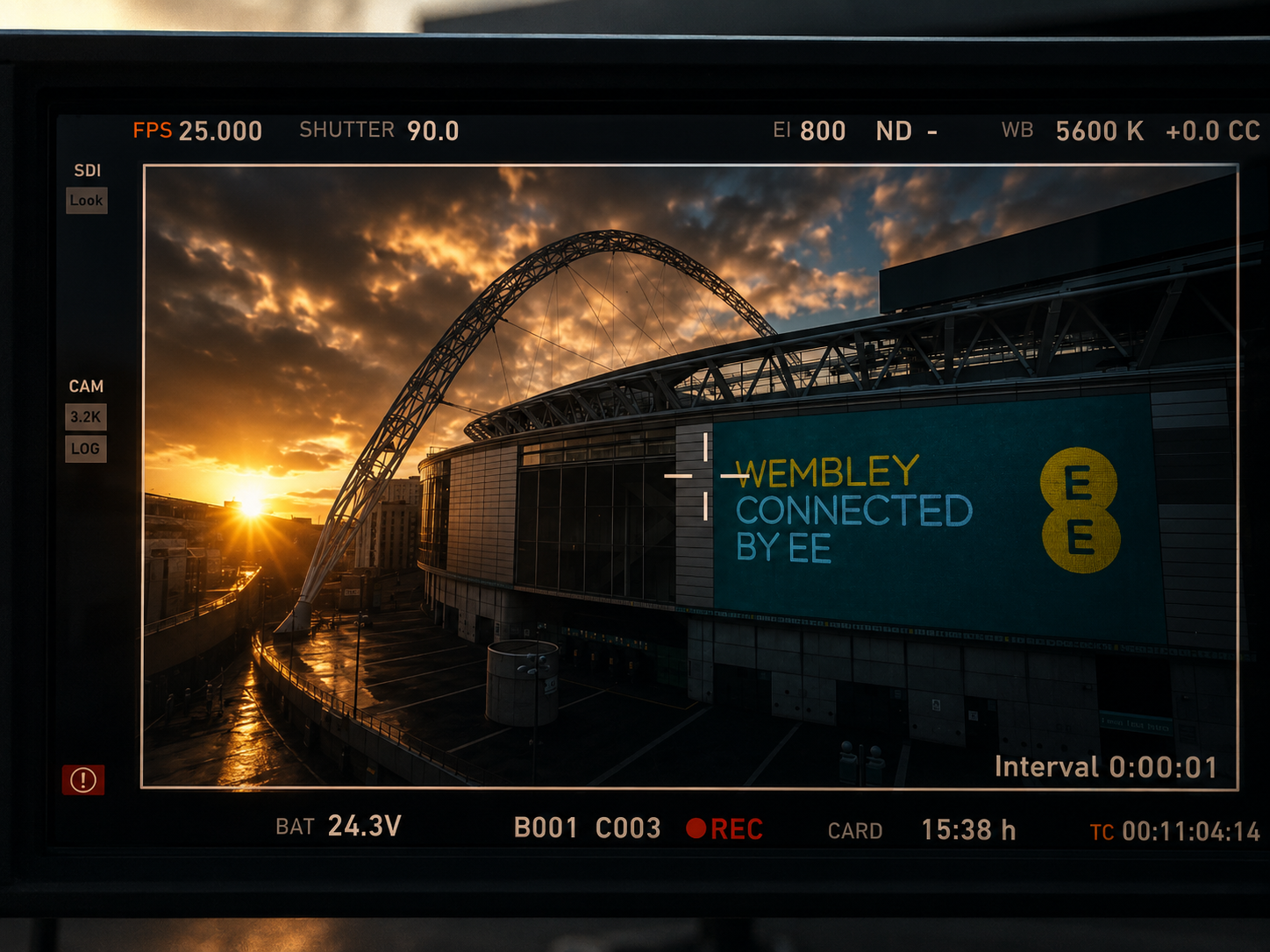 A camera viewfinder showing a sunset with partly cloudy sky over Wembley Stadium, with a digital screen displaying the words "WEMBLEY CONNECTED BY EE" and the EE logo.